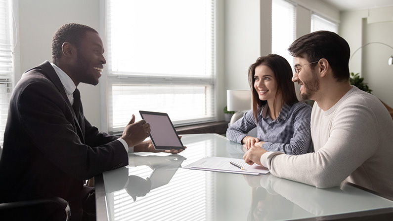 Happy african american businessman showing mockup on tablet. Smiling successful business manager talking making deal with customer presentation. Professional employee presenting product to couple.